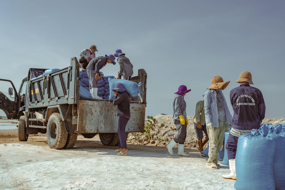Team of workers unloading blue salt bags from a truck under a clear sky.